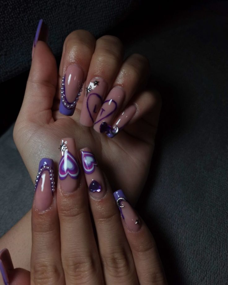 Glamorous Purple and Nude Nail Design with Heart Motifs and Shimmering Gems.