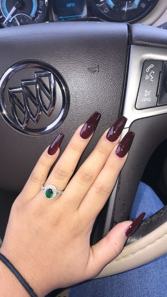 Chic Almond-Shaped Dark Burgundy Nails with Emerald Accent Ring: A Bold and Elegant Design.