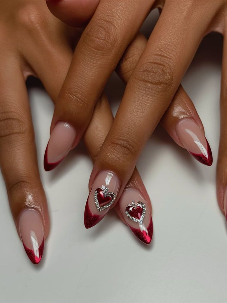 Elegant Almond-Shaped Nail Design: Nude Base with Vibrant Red Tips and Glamorous Heart Motifs.