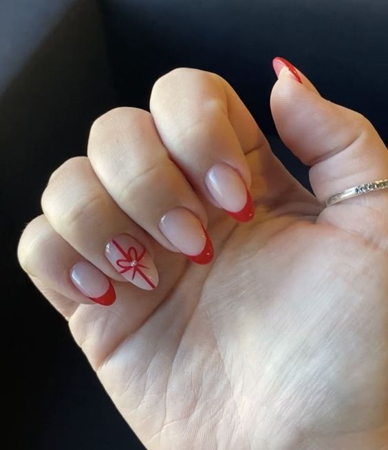 Chic Nude and Red Nail Design with Festive Ribbon Accents for Special Occasions.