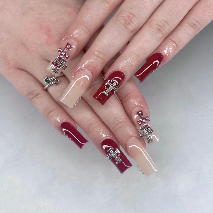 Elegant Deep Red and Nude Nail Design with Metallic Charms and Rhinestones.