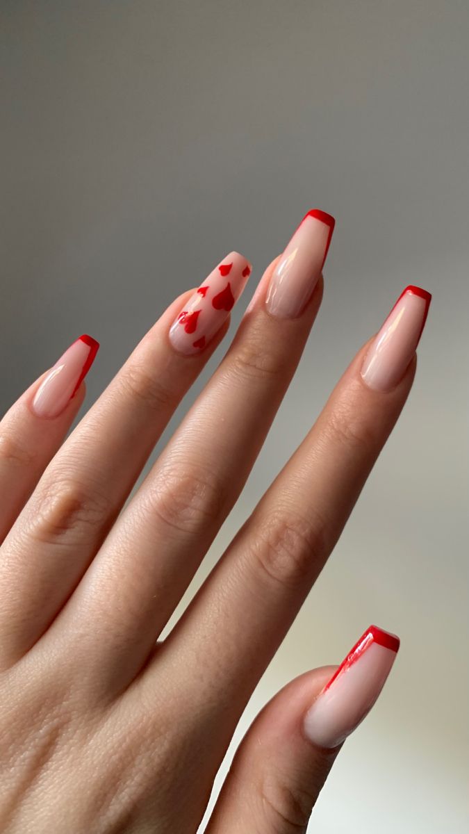 Chic Nail Design: Elegant Nude Base with Red French Tips and Charming Heart Patterns.