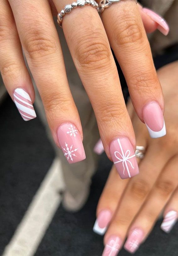 Chic Holiday Nail Design: Soft Pink and White with Snowflakes, Bows, and Striped Accents.