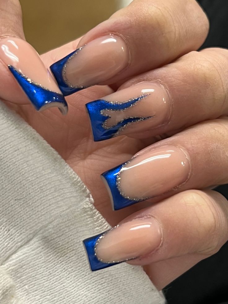 Striking Bold Nail Design: Deep Blue Tips on Nude Base with Glossy Finish and Metallic Accents.