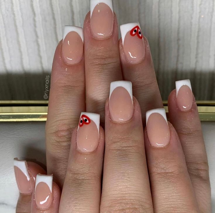 Chic French Tip Manicure with Nude and White Polish Accented by Playful Red Hearts.