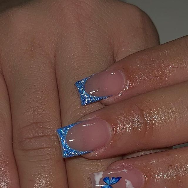 Chic Nail Art: Glossy Nude Base with Sparkling Blue Tips and Playful Butterfly Accents.