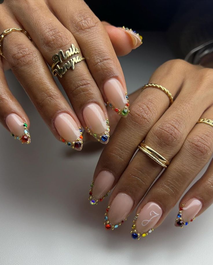 Chic Nude Nail Design with Gemstone-Accented Tips and Dainty Gold Jewelry.