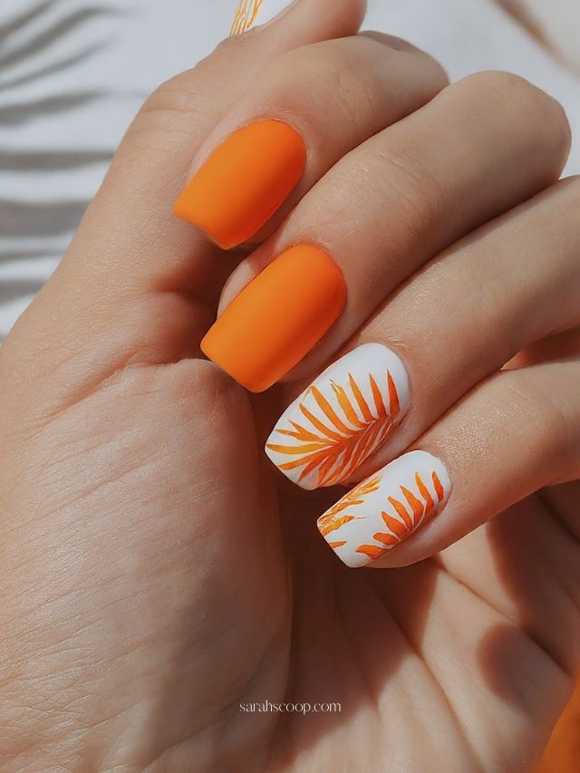 Vibrant Tropical Nail Design: Bold Orange Matte with Delicate White Leaf Patterns.