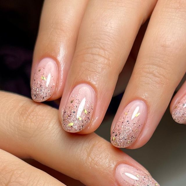 Chic Glittering Ombre Nails: Soft Pink Base with Sparkly Nude Tips and Gold Accents.