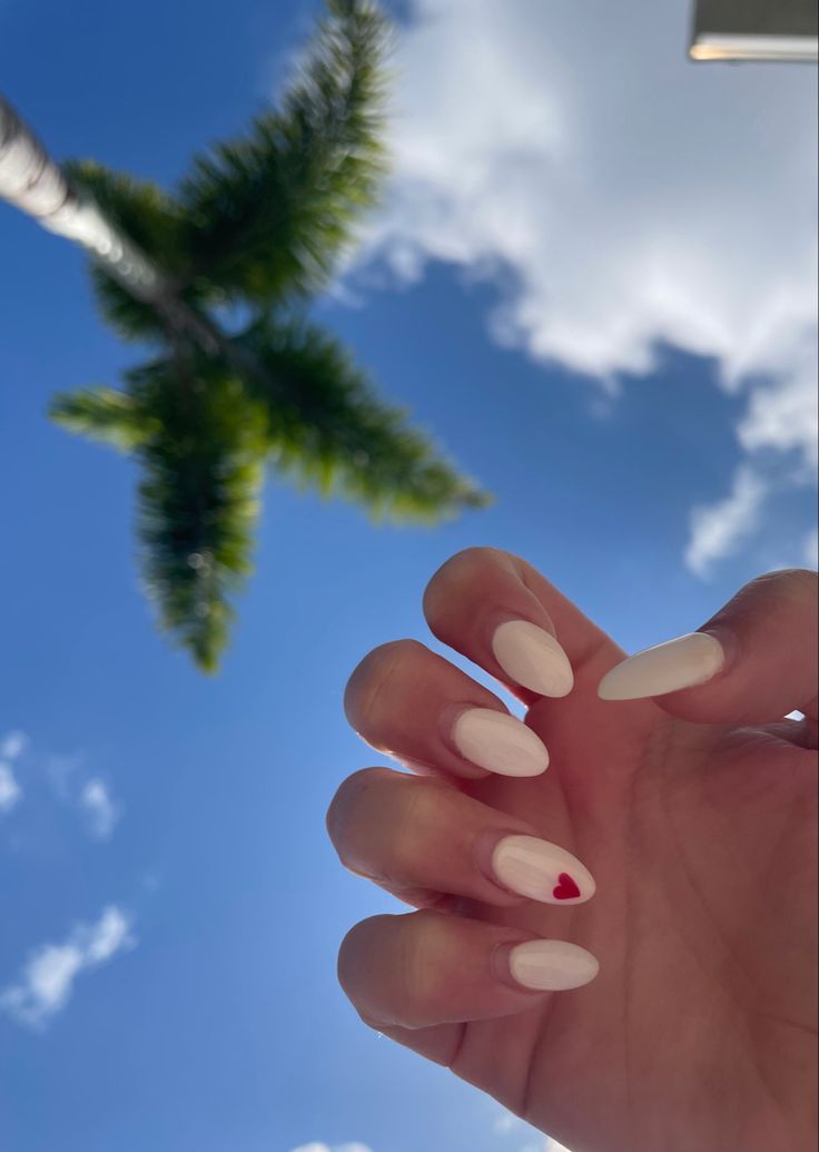 Chic Outdoor Nail Design: White Polish with Playful Red Heart Accent on Almond-Shaped Nails