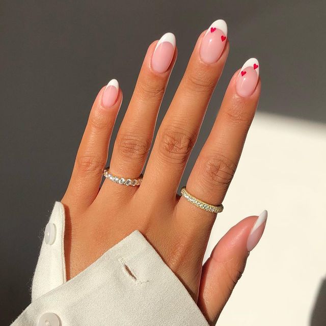 Chic Pink and White Nail Design with Whimsical Red Hearts and Delicate Rings.