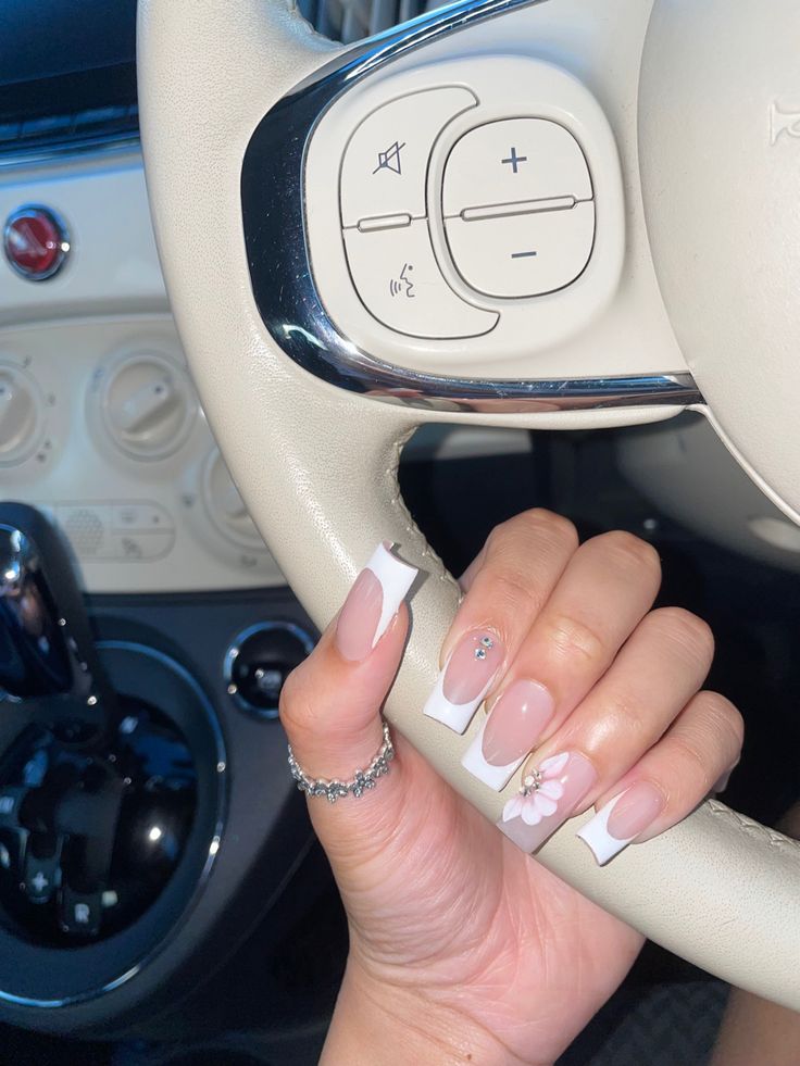 Chic Nude and White Nail Design with Floral Accents and Rhinestones for a Trendy Look.