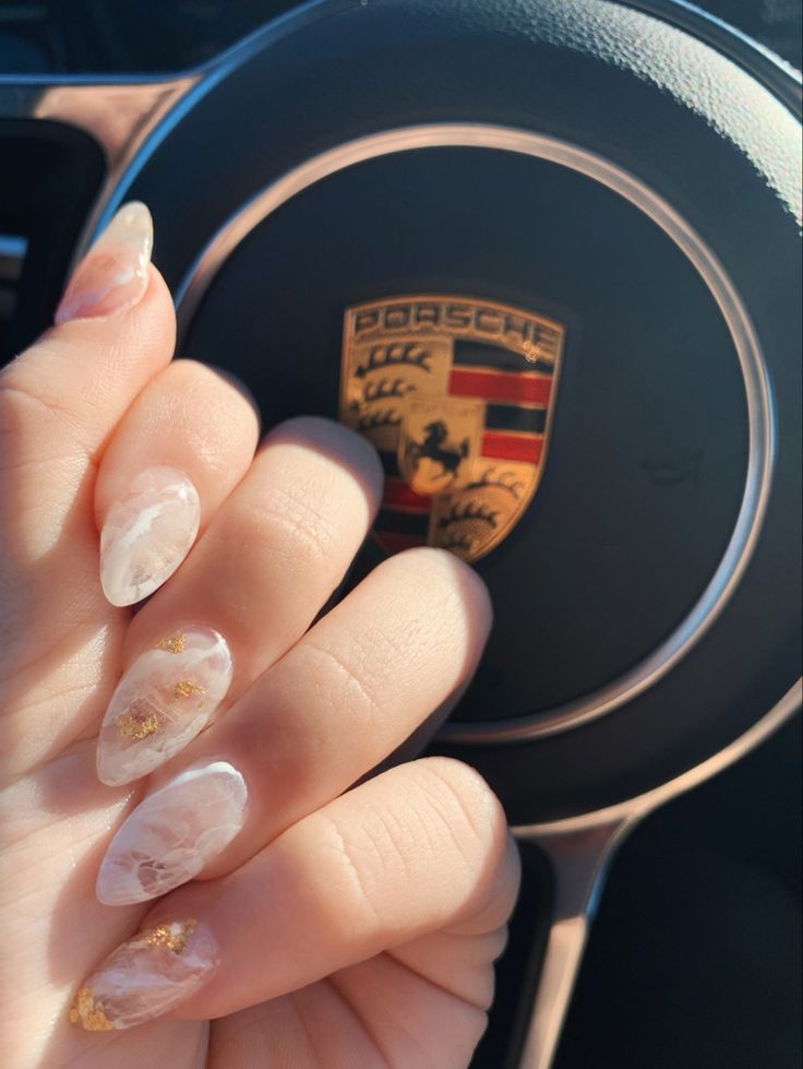 Sophisticated Almond-Shaped Nails with Marbled Pink and Gold Accents Enhance Luxurious Car Interior.