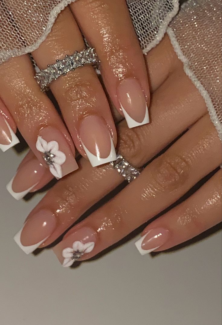 Elegant French Tip Nails with Floral Accents and Glamorous Touches.