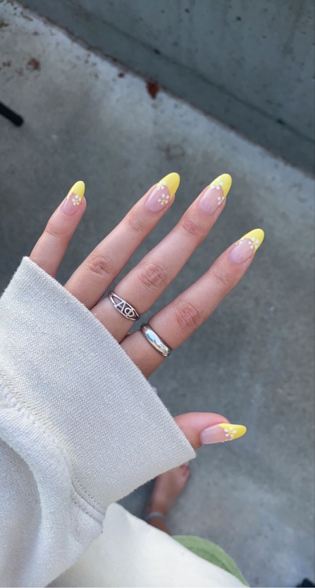 Cheerful Spring/Summer Nail Design: Vibrant Yellow Tips with White Floral Accents and Elegant Silver Rings.