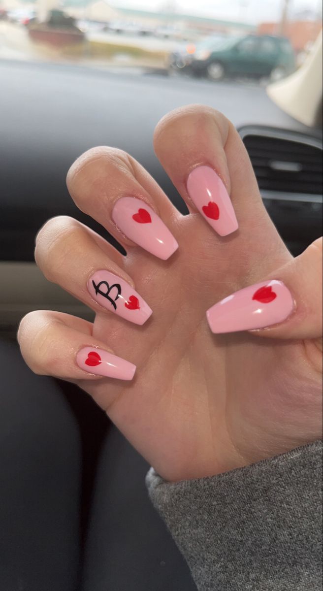 Delightful pink nail design with playful red hearts and a bold black accent for a whimsical, romantic touch.