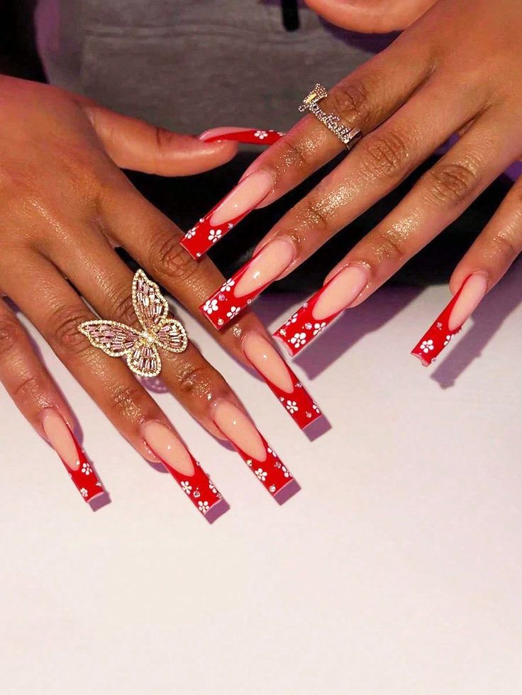 Elegant Coffin-Shaped Nail Design with Red and Nude Palette and Floral Patterns, Accentuated by a Butterfly Ring.