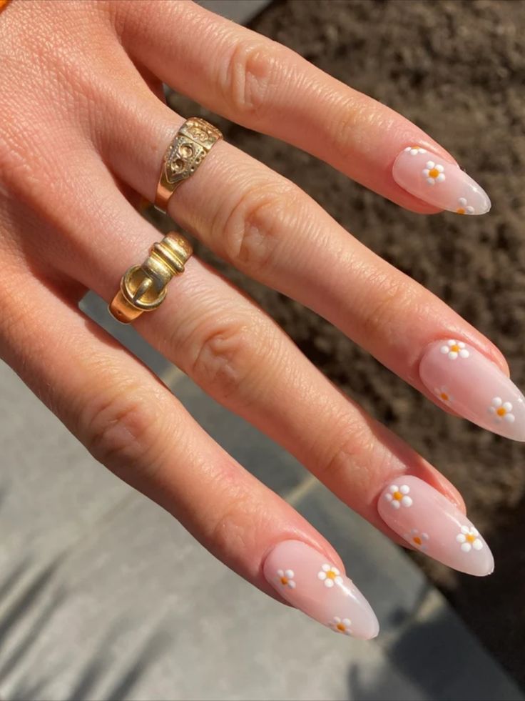 Chic Almond-Shaped Nails with Soft Pink Base and Floral Accents, Enhanced by Gold Rings.