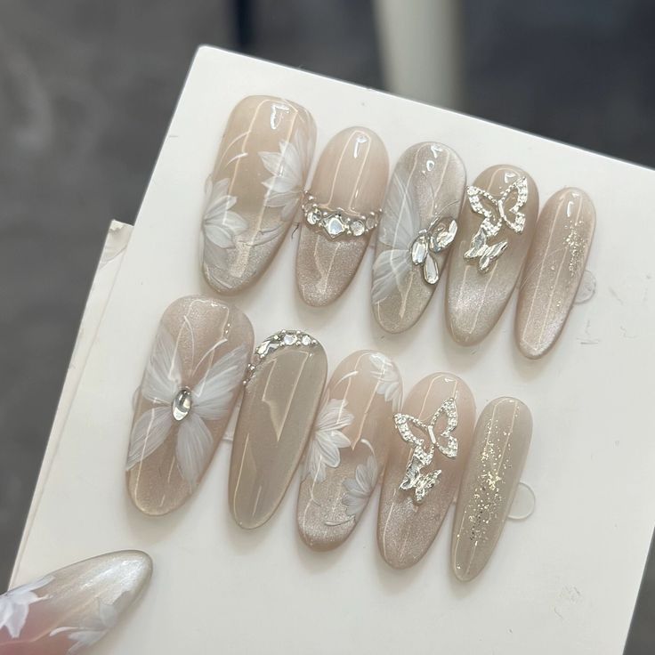 Chic Nude Nail Design with Whimsical Floral Accents and Glamorous Glitter