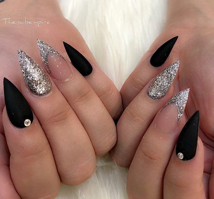 Elegant Matte Black and Shimmering Silver Glitter Nail Design with Striking Pointed Shapes and Accent Stones.