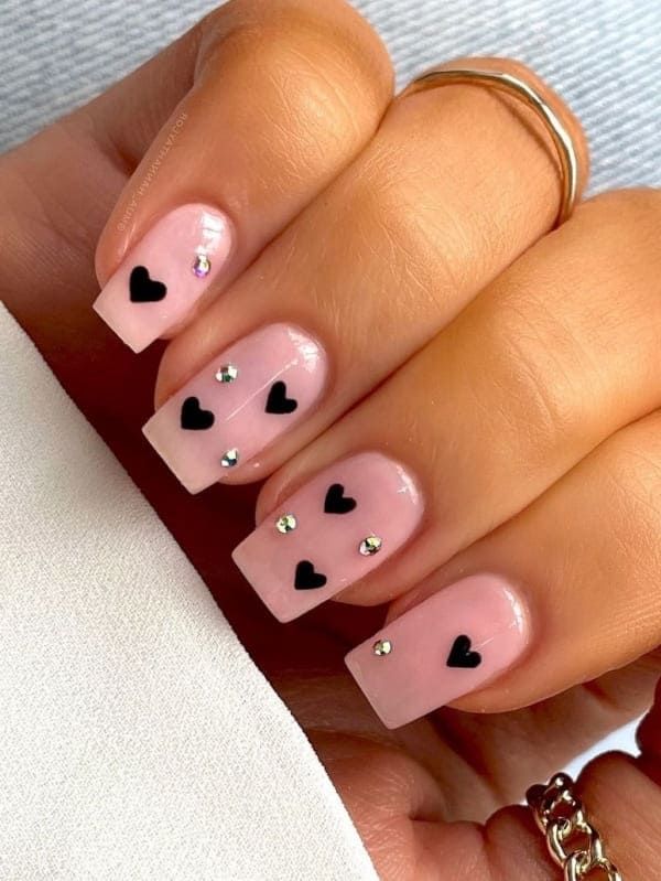 Trendy Playful Nail Design: Soft Pink Base with Black Hearts and Sparkling Rhinestones