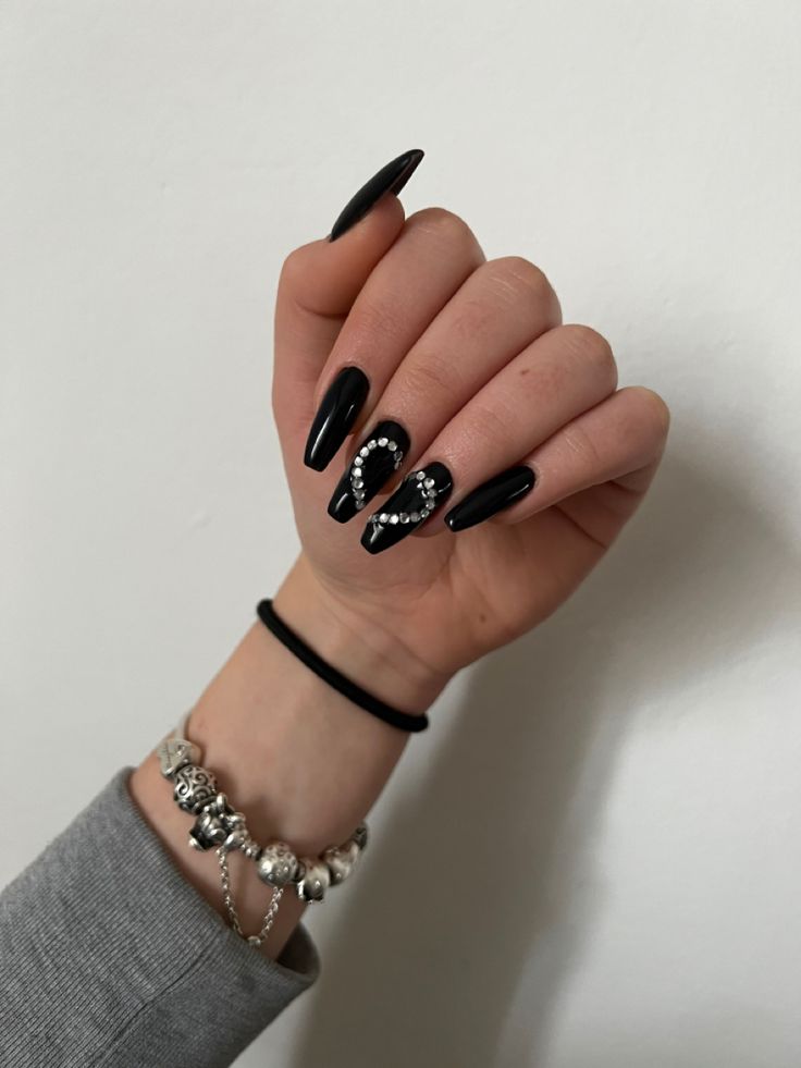 Sophisticated Almond-Shaped Black Nail Design with Glossy Finish and Jewel Accents.