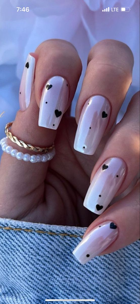 Chic White Nail Design with Playful Black Heart Accents for a Trendy, Romantic Look.