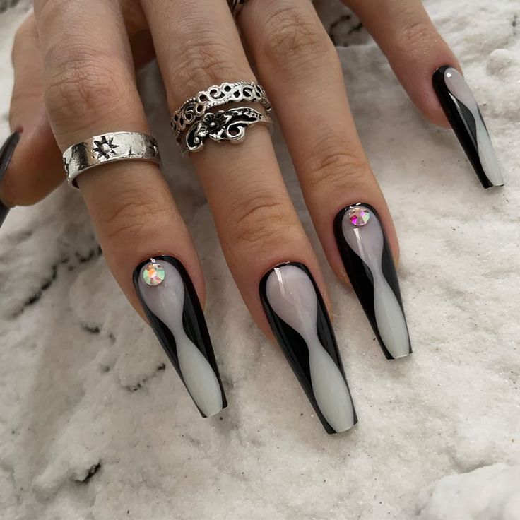 Elegant Black and White Swirl Nail Design with Iridescent Gems and Chic Silver Rings.