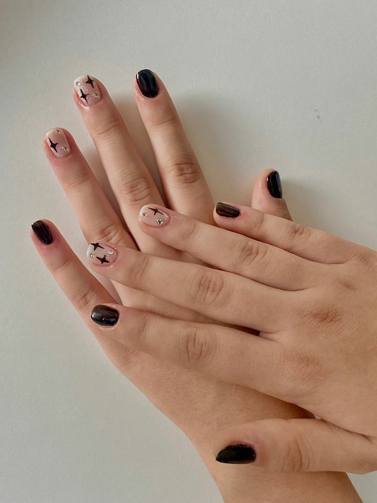 Chic Black and Nude Nail Design with Star Patterns and Subtle Embellishments.