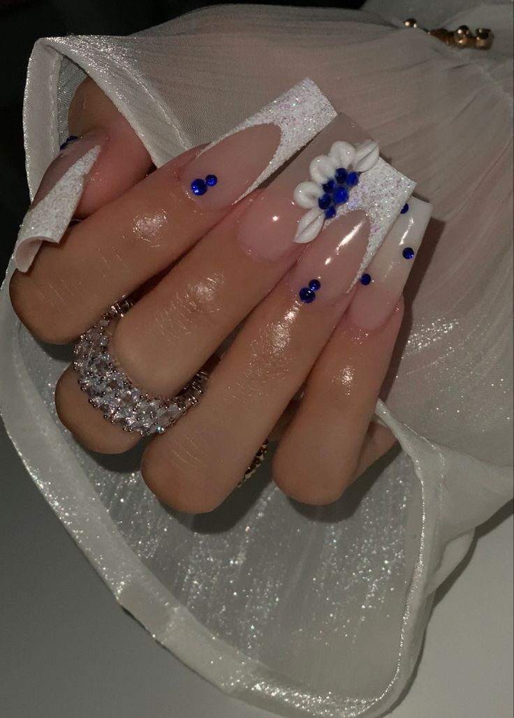 Glamorous Long Acrylic Nail Design with Floral Accents and Blue Gem Contrast.