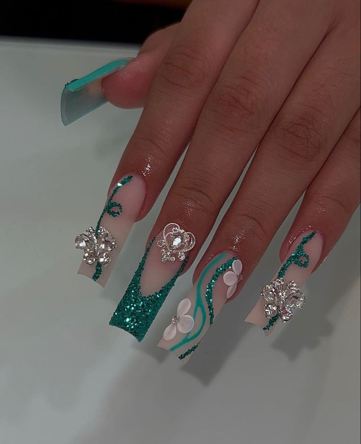 Chic Turquoise Glitter Nail Design with Floral Accents and Gemstone Embellishments.