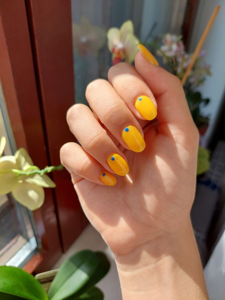 Cheerful Yellow Nail Design with Glossy Finish and Elegant Blue Gemstones.