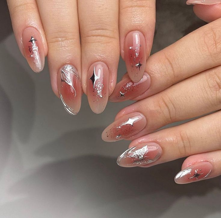 Sophisticated Nail Design with Nude-Pink Gradient, Glitter Accents, Silver Leaf Motifs, and Star Embellishments.