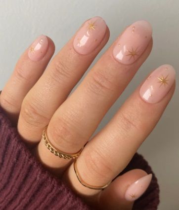 Chic Nude Nail Design with Delicate Gold Star Patterns and Shiny Finish.