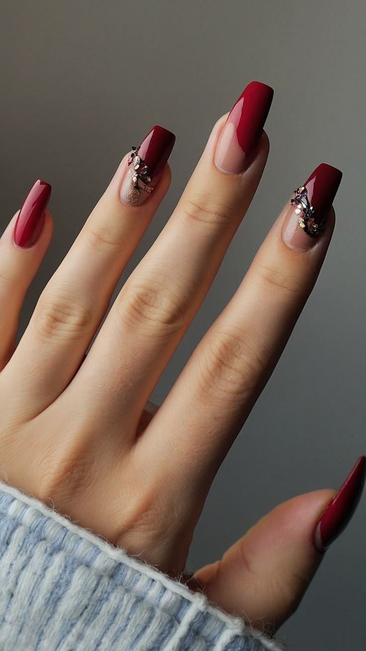 Luxurious Crimson and Nude Nail Design with Intricate Embellishments.