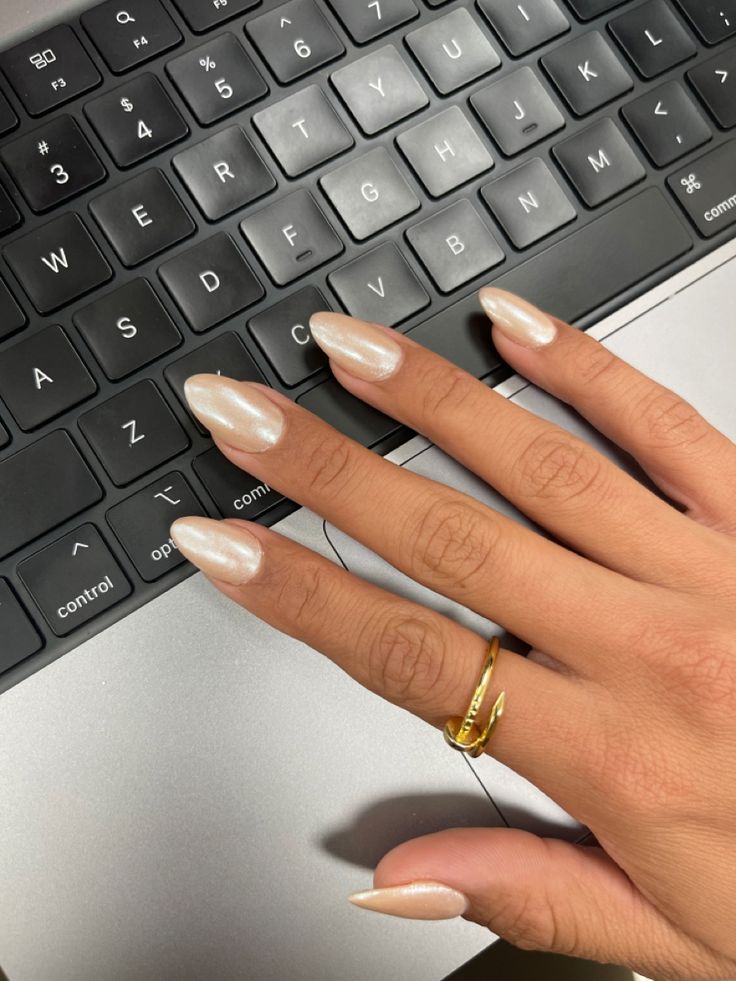 Elegant Almond-Shaped Nails with Pearlescent Finish and Delicate Gold Ring for a Sophisticated Look.