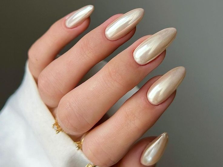 Chic Almond-Shaped Nails with Shimmering Nude Polish and Delicate Gold Rings.