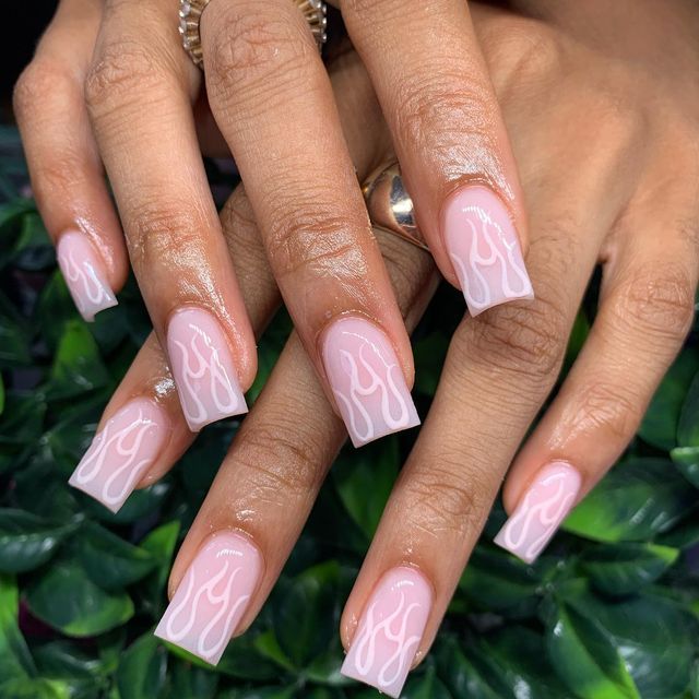 Chic Flame-Inspired Nail Design with Soft Pink Base and Elegant White Patterns.