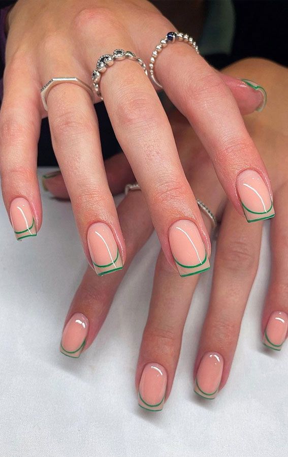 Modern French Manicure: Soft Nude Base with Vibrant Green Tips and Delicate Silver Accents.