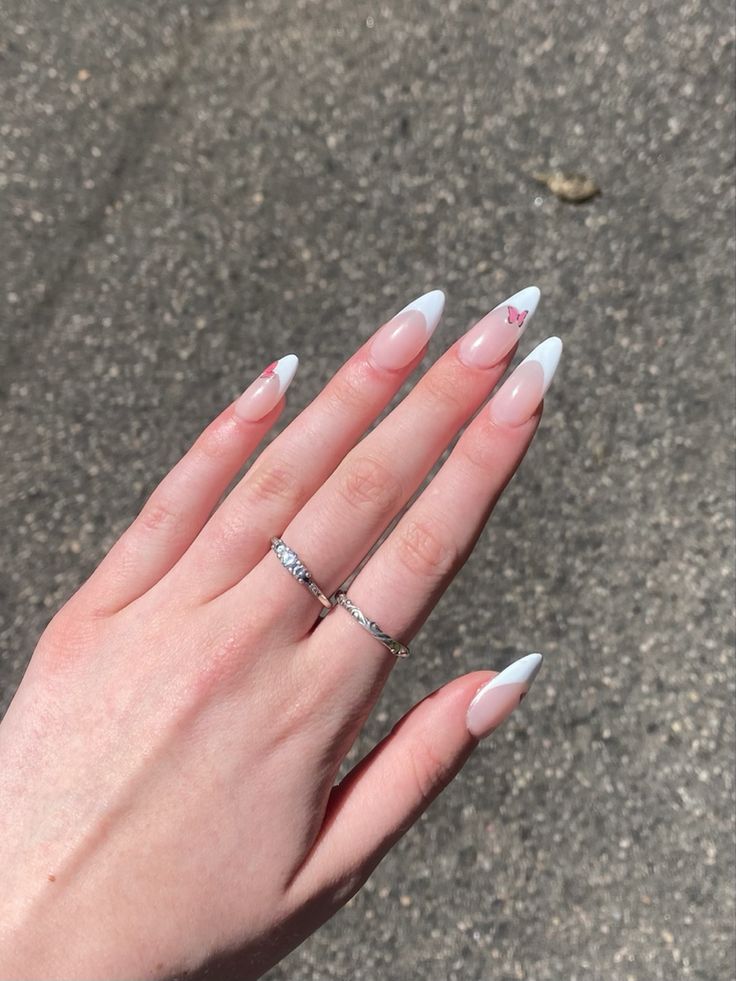 Sophisticated Almond-Shaped Nails with Pink and White Tips, Delicate Butterfly Motif, and Minimalist Silver Rings.