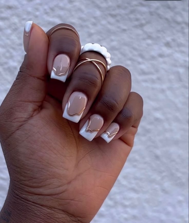 Sophisticated Nude and White Nail Design with Gold Accents and Minimalistic Rings.