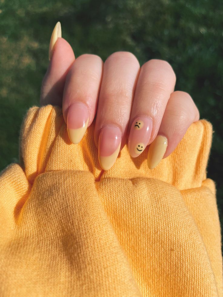 Charming Yellow and Nude Nail Design with Playful Smiley Face Accent for a Cheerful Spring/Summer Look.