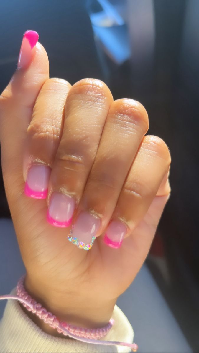 Playful Pink Nail Design: Soft and Hot Pink Tips with Sparkling Gem Accent.