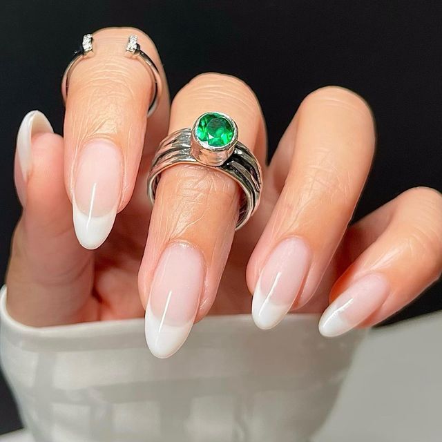 Sophisticated French Tip Manicure with Nude and White Shades, Enhanced by Green Gemstone and Silver Rings.