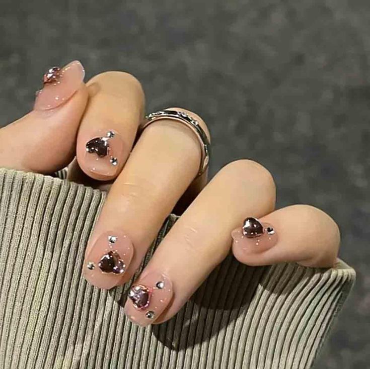 Chic Nude Nail Design with Sparkling Heart-Shaped and Gem Accents.