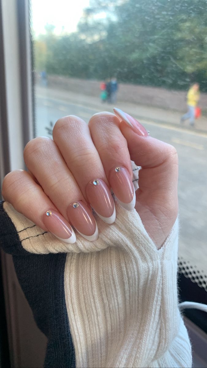 Chic Nude and White Nail Design with Subtle French Tips and Rhinestone Accents.