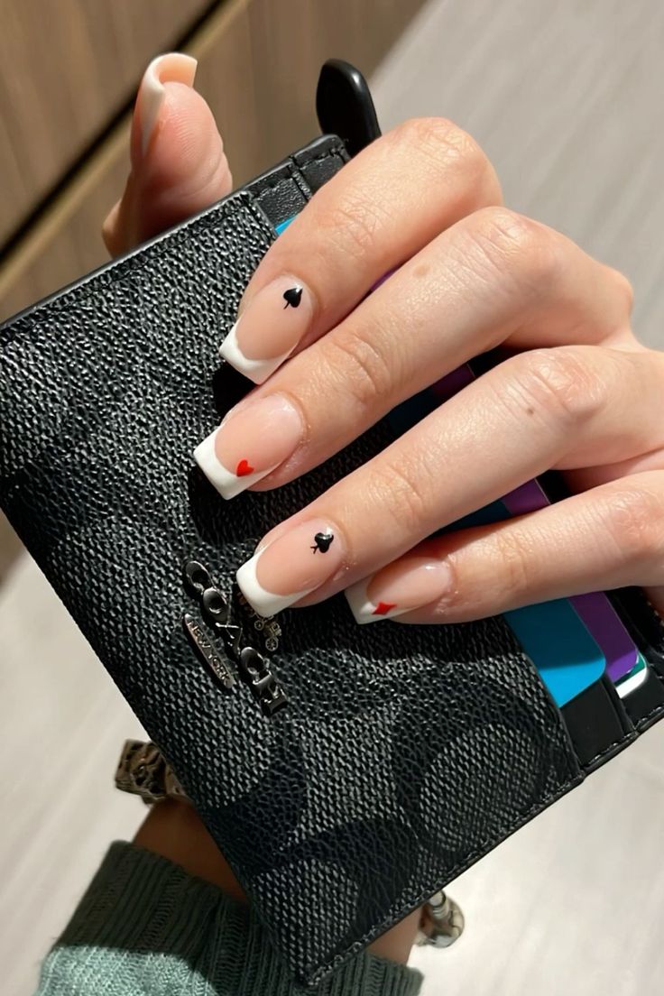 Chic French Manicure with Whimsical Red and Black Heart Accents.