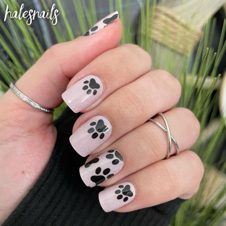 Playful Paw Print Nail Design: Whimsical Light Pink Base with Bold Black Accents for Animal Lovers.