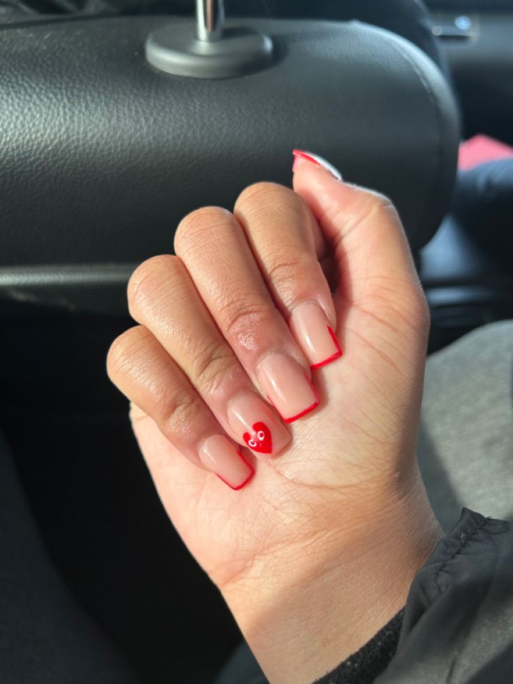 Chic Nail Design: Natural Base with Vibrant Red Tips and Whimsical Heart Accent.