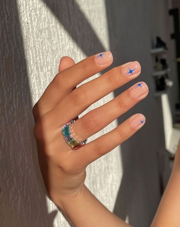 Chic Natural Nude Manicure with Playful Blue Star Accents and Vibrant Multi-Colored Ring.